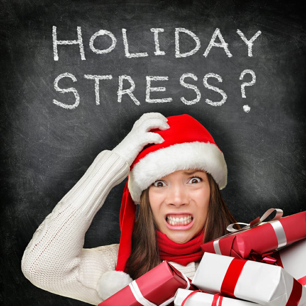 Christmas holiday stress. Stressed woman shopping for gifts holding christmas presents wearing red santa hat looking angry and distressed with funny expression on black chalkboard background.